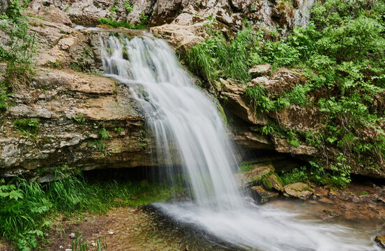 view of a small mountain river waterfall among large cobblestones from a cliff.
