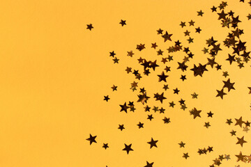 Golden stars confetti scattered on a yellow background. Place for text.