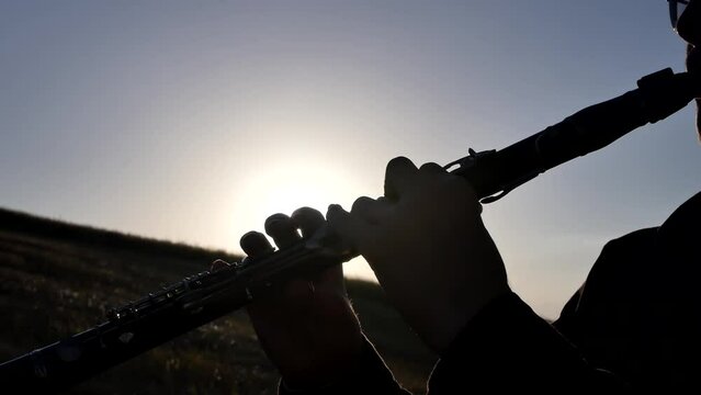 Silhouette of a musician man at sunset in the mountains playing the clarinet pressing his fingers on the keys of a wind instrument. Close-up of a clarinetist's hands playing classical music