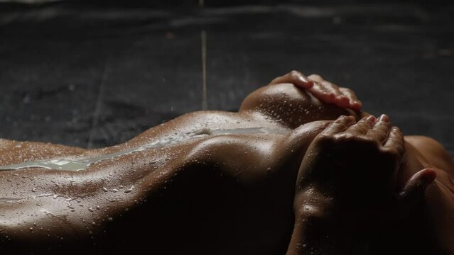 Beautiful tanned body close-up on a black background. Milk is poured on the girl's body close-up