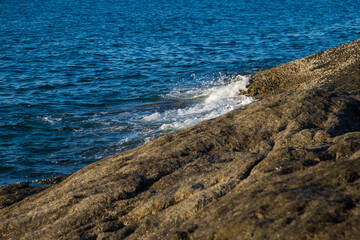 Sea wave splash on rocky beach sunny day morning sunrise