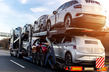 Tow truck car carrier semi trailer on highway carrying batch of new wrapped electric SUVs on...