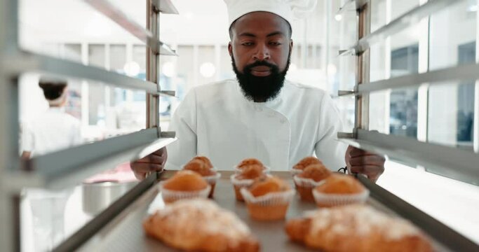 Muffins, pastry chef and a man in a restaurant kitchen for baking job. Happy professional black person working with food at work with hotel or bakery trolley for production, breakfast or service