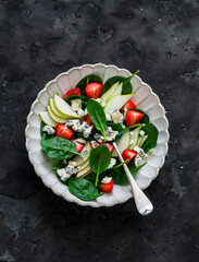 Pear, spinach, blue cheese, strawberry salad on a dark background, top view