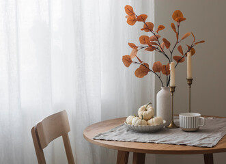 Autumn home interior in the living room - around wooden table, a chair, a bouquet of autumn leaves...