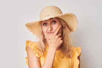 Portrait of clever mature woman in summer yellow clothes touching chin thinking chooses doubts isolated on white studio background with copy space.