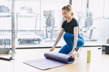 Fototapeta premium Fitness woman in sport club studio with yoga mat. Young woman roll pilates mat at a fitness training class.