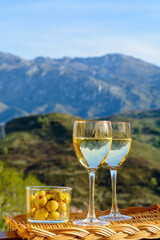 Glasses of dry white wine and spanish tapas olives in bowl with mountains peaks on background in...