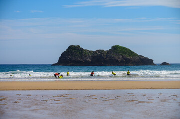 Young surfers train on Playa de Palombina Las Camaras in Celorio, Green coast of Asturias, North Spain with sandy beaches, cliffs, hidden caves, green fields and mountains