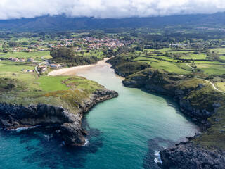 Fototapeta na wymiar Aerial view on Playa de Poo during low tide near Llanes, Green coast of Asturias, North Spain with sandy beaches, cliffs, hidden caves, green fields and mountains.