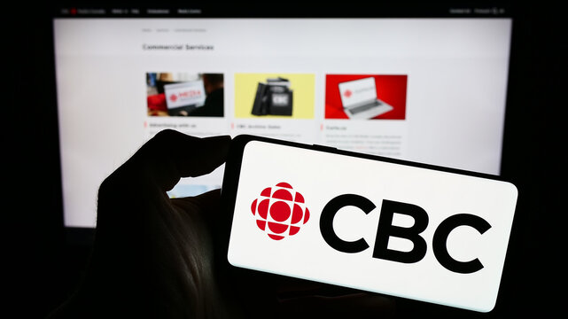 Stuttgart, Germany - 08-30-2023: Person holding cellphone with logo of Canadian Broadcasting Corporation (CBC) on screen in front of webpage. Focus on phone display.