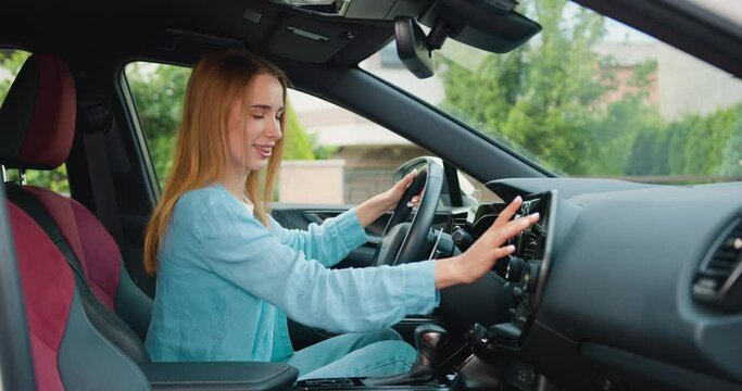 Young woman is sitting in the driver's seat using a touch display screen multimedia device in sporty car driven. Attaractive girl tasting new vehicle functions.