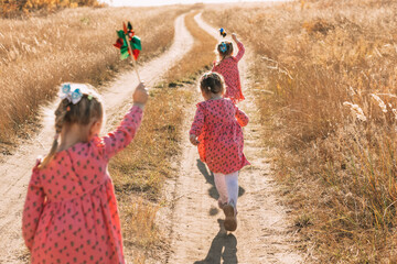 Playing in the wind: triplet girls run towards adventures with windmills on a warm autumn day,...
