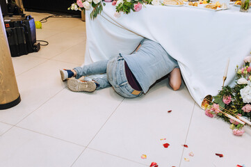 A drunken man hides under a tablecloth in a restaurant at a banquet. Photography, lifestyle.