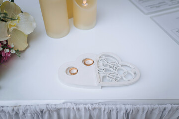 The gold rings are in a heart-shaped wooden box on a white table with the inscription "Mr. and Mrs.". Wedding photography, accessories, details.