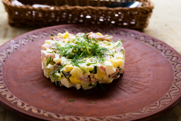 Traditional Russian salad with peas and mayonnaise, served in a cylinder on a clay plate