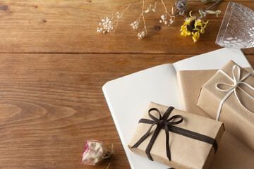 Dried flowers such as roses and sunflowers on a wooden table, a box of gifts in natural taste and a glass with a notebook, a book and a transparent