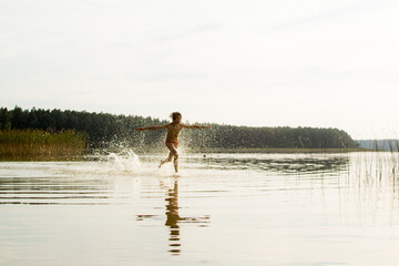 Fototapeta na wymiar A slender guy child teenager runs along the water along the coast at sunset, splashing from the water.