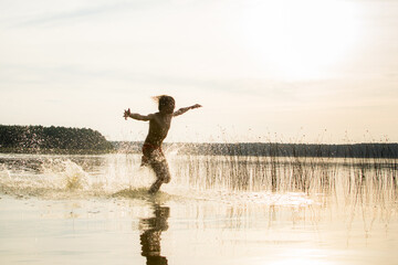 A slender guy child teenager runs along the water along the coast at sunset, splashing from the water.