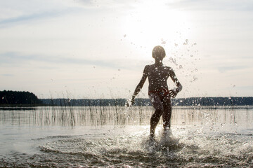 A slender guy child teenager runs along the water along the coast at sunset, splashing from the water.