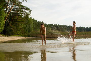 A slender guy child teenager runs along the water along the coast at sunset, splashing from the water.