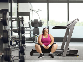 Fototapeta na wymiar Smiling overweight woman resting on a treadmill at a gym