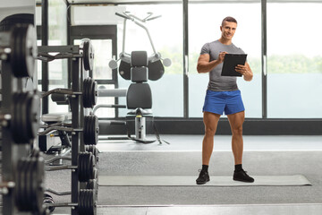Fototapeta na wymiar Full length portrait of a fitness instructor writing a document in a gym