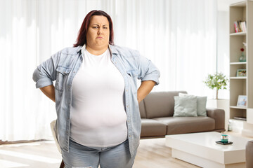 Grumpy overweight woman standing with hands on waist at home