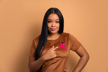 confident afro brazilian woman showing pink ribbon in all beige colors. breast cancer, awareness...