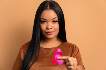 hands of african american woman showing pink ribbon in all beige colors. breast cancer, awareness...