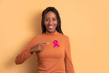 happy black young woman showing pink ribbon in studio shot. breast cancer, awareness concept.
