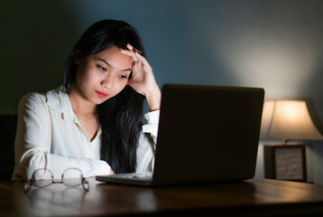 Overworked female tired holds her head in hands while working and studying on a personal computer.