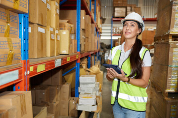 portrait worker working on tablet and looking at cardboard box on shelf in warehouse storage