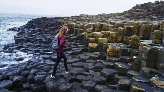  Giants Causeway woman walking next to coastline with waves crashing