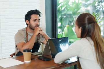 Asian man sitting on chin showing boredom in front of laptop computer Between accounting income and expenses of a small family business, a coffee shop, and calling his wife to watch the screen.