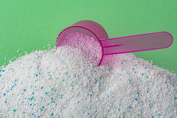 Washing powder in a plastic spoon on a green background
