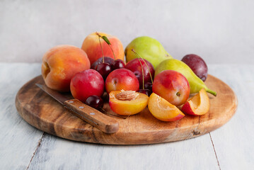 On a light table on a wooden board a knife, plums, peaches and pears. Healthy food concept.