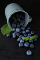 Blurred image of blueberries and a cup on a dark background.