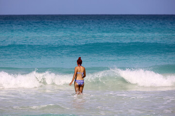 Girl in swimsuit going to swim in azure sea water. Beach vacation on sunny coast