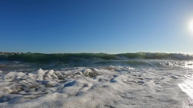 Waves crashing into the camera in slow motion at the beach on a sunny day in California.
