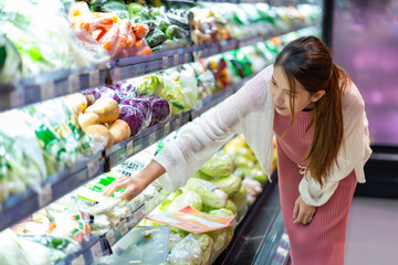 Asian woman who is four months pregnant. Choosing food meticulously in the supermarket