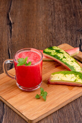 Watermelon juice in a glass mug with mint leaves and watermelon rinds on a cutting board.