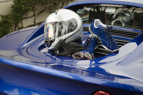A lifestyle shot of a British sports car with driving shoes, driving gloves, sunglasses, and a racing helmet arranged on the engine cover