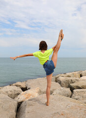 girl balancing on one leg while doing gymnastics on the rocks by the sea