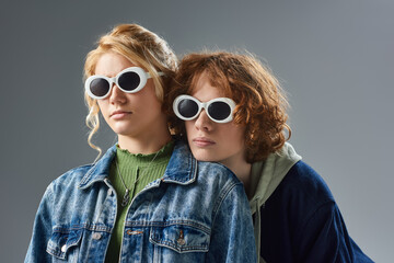 portrait of redhead teen guy and blonde girlfriend in sunglasses and stylish outfit posing on grey