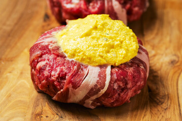 Two big uncooked beef burgers wrapped with bacon slice and portion of cheese on wooden board. Premium meat product. High quality cheeseburger.