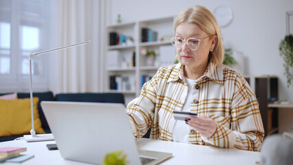 Woman in her 50s using credit card to make a payment on laptop, online shopping