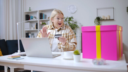 Senior woman receiving a large pink gift box after paying with a credit card, online shopping