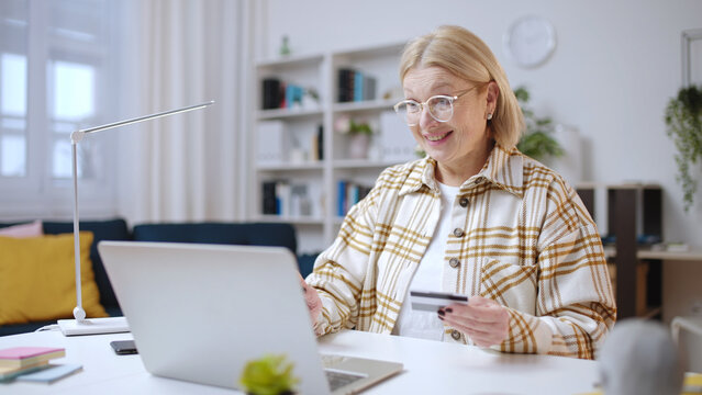 Excited senior woman paying for a purchase online with a credit card, cashless payment
