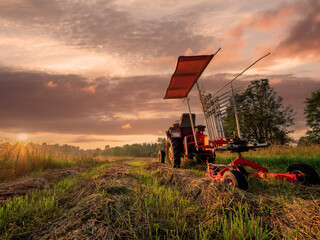 Fototapeta premium Old rusty tractor with grass cutting machine in a agriculture field with tall grass at stunning sunrise. Farming industry. Beautiful nature scene at special time. Nobody.